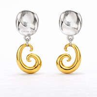 COCOA ARI two-tone earrings with sculpted silver studs and gold swirl pendants on white background