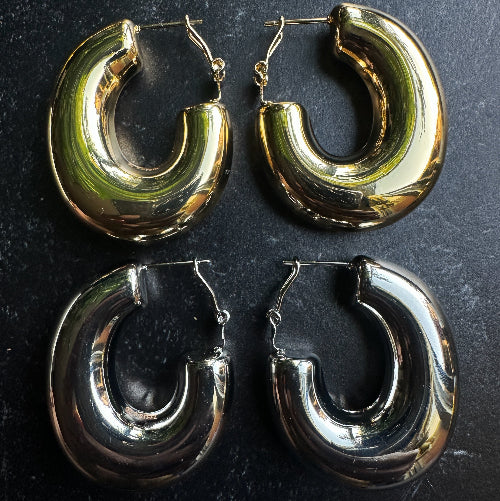 Two pairs of hoop earrings, one gold and one silver, on a dark surface.