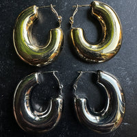 Two pairs of hoop earrings, one gold and one silver, on a dark surface.