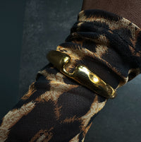 Gold bracelet on a patterned arm against a dark background