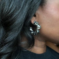 Close-up of an ear wearing a silver leaf-shaped earring with dark hair.