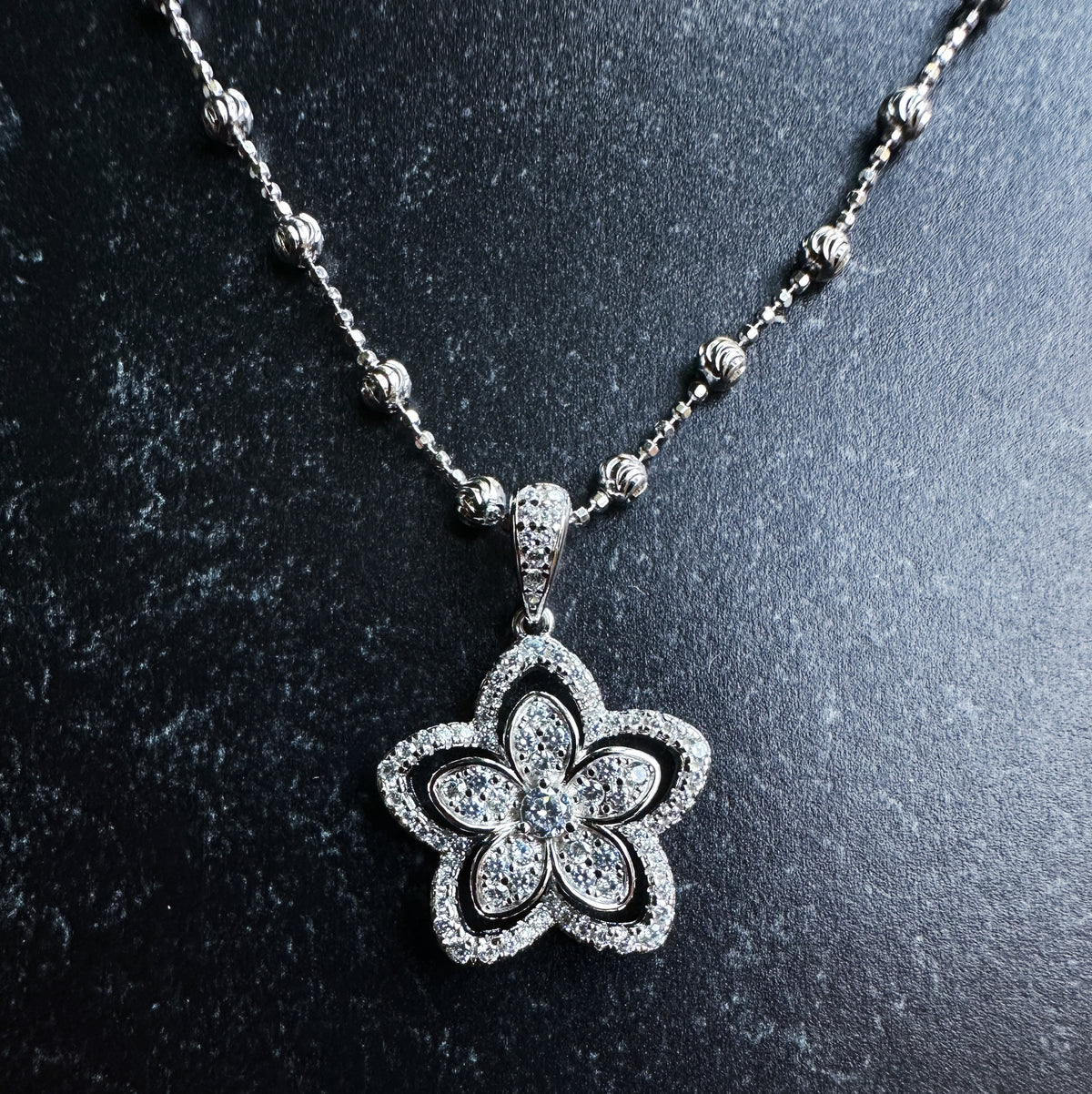 Silver flower-shaped pendant on a chain against a dark background