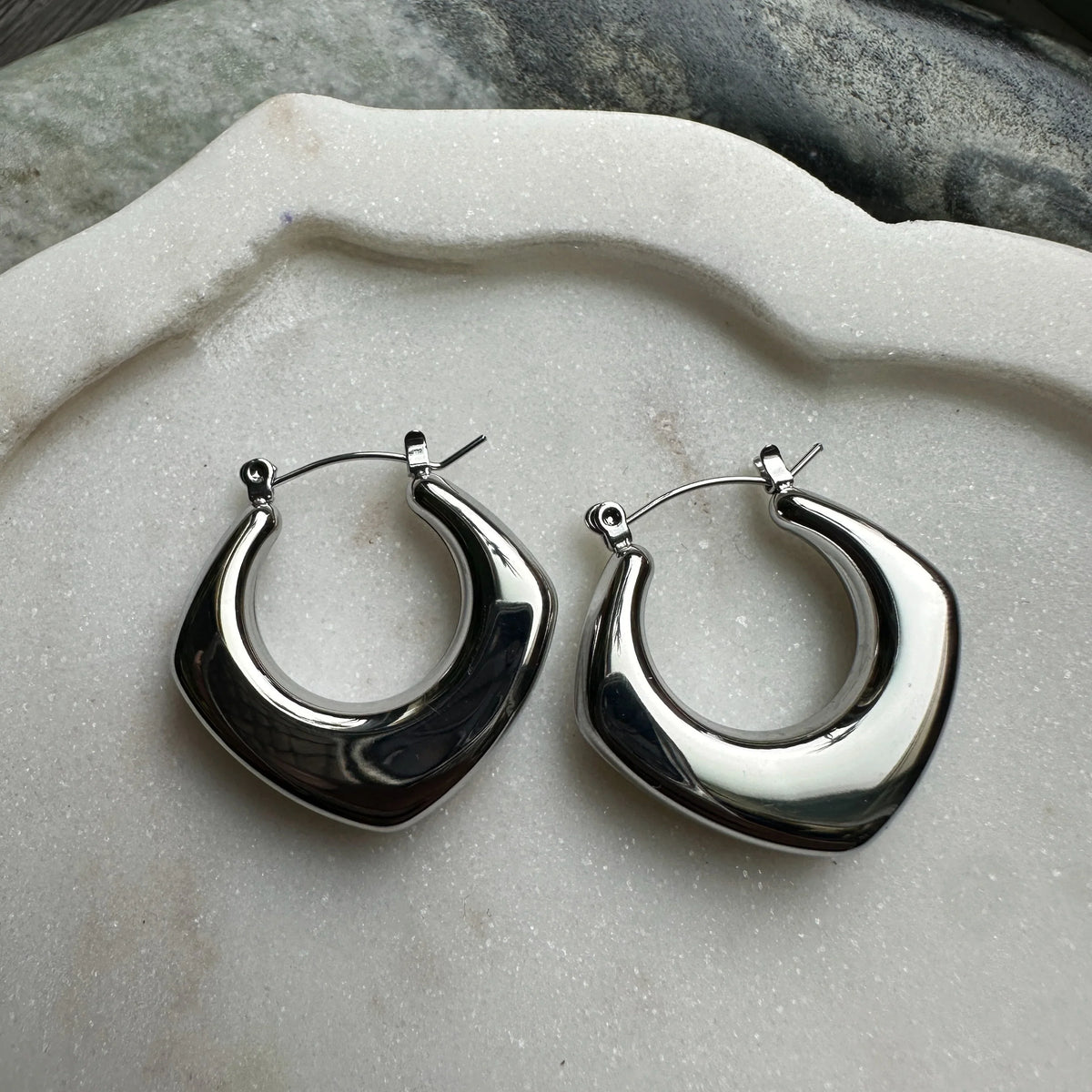 Silver hoop earrings on a textured stone surface