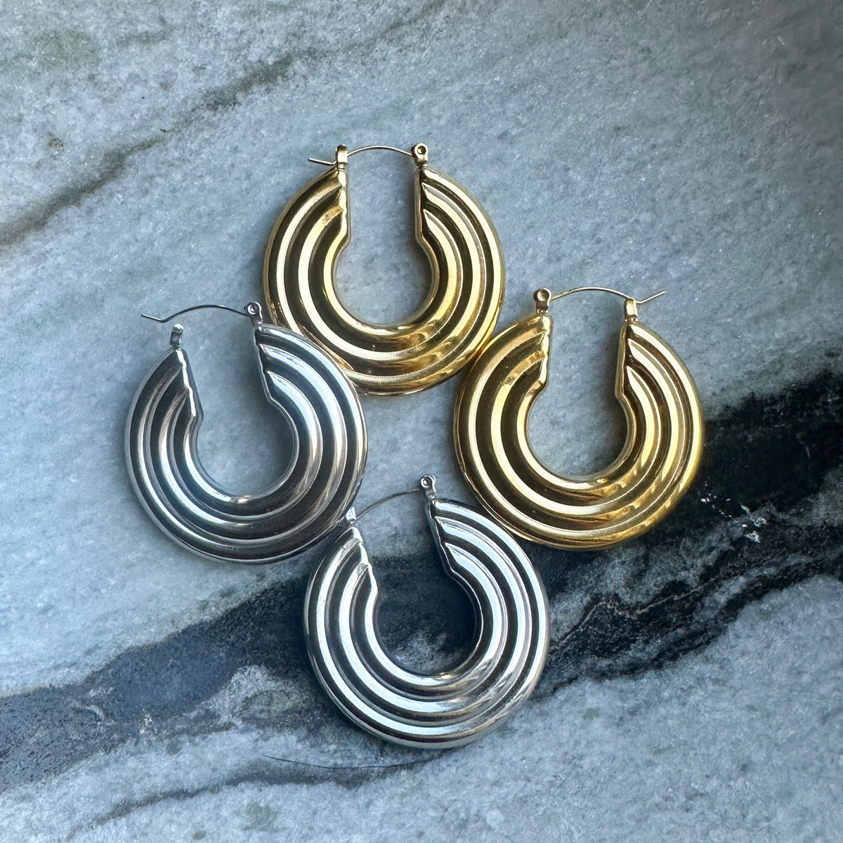Pair of gold and silver hoop earrings on a textured stone surface