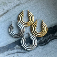 Pair of gold and silver hoop earrings on a textured stone surface