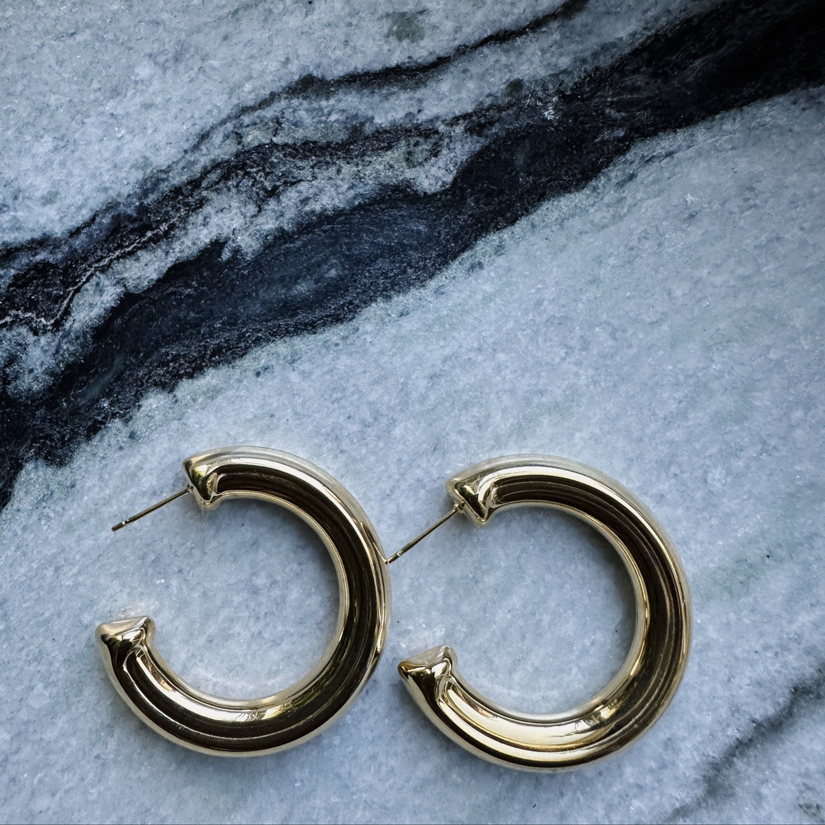 Gold hoop earrings on a marble surface