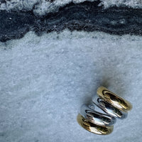 Two gold and silver earrings on a textured surface