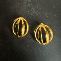 Pair of gold dome orbit earrings on a dark textured background