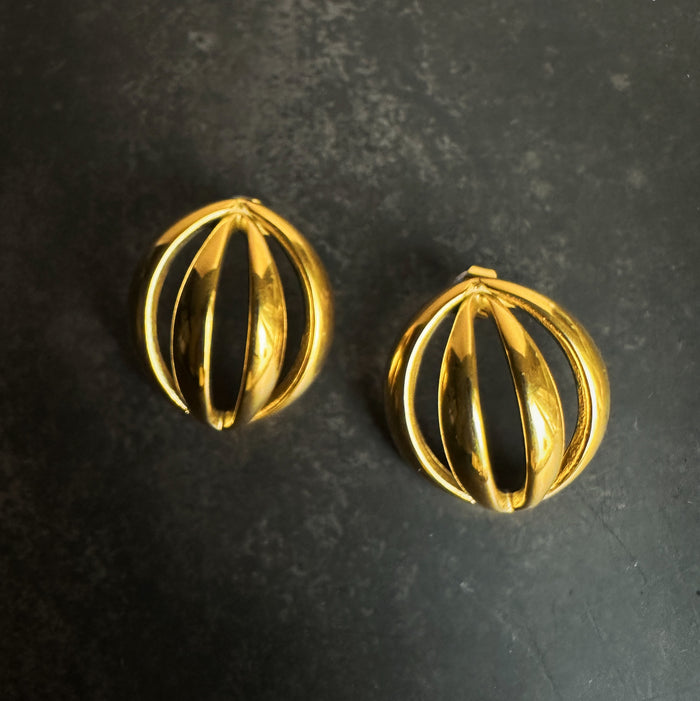 Pair of gold dome orbit earrings on a dark textured background