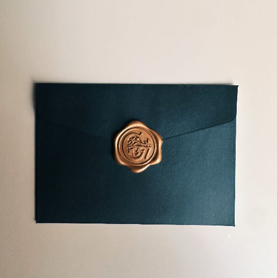 Dark green envelope with a gold wax seal on a beige background