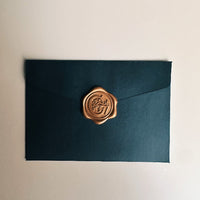 Dark green envelope with a gold wax seal on a beige background