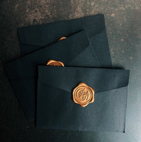 Three dark blue envelopes with gold wax seals on a textured surface