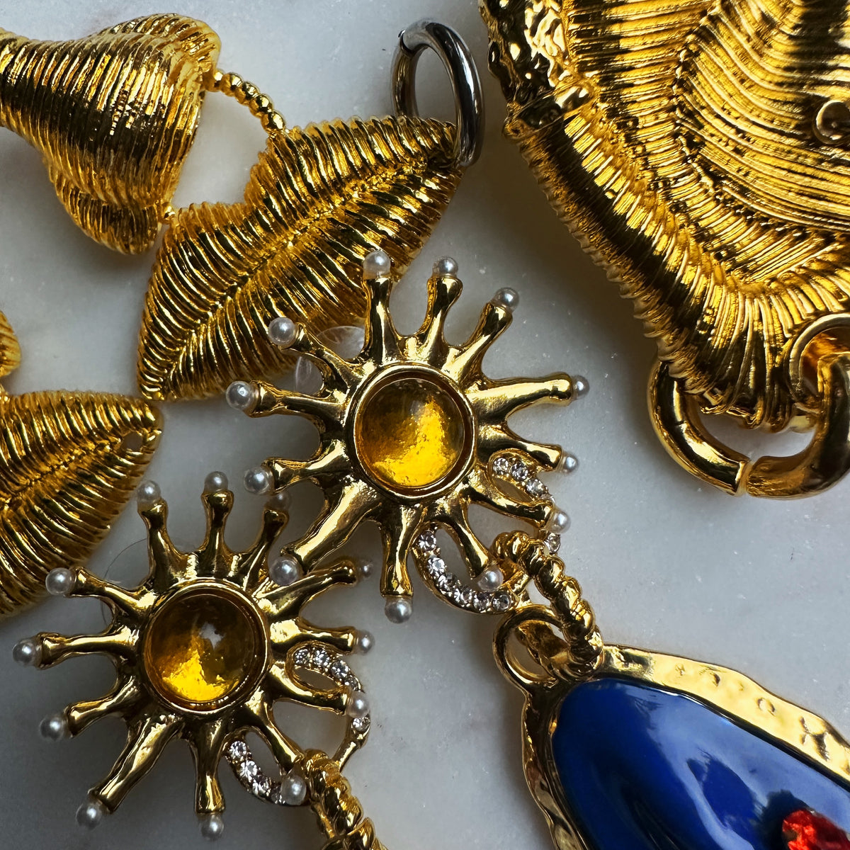 Gold jewelry with sun design and blue stone on a light background