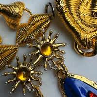 Gold jewelry with sun design and blue stone on a light background