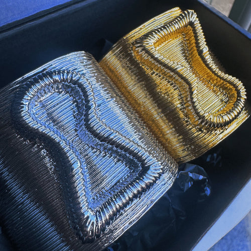 Two embroidered fabric samples, one blue and one gold, on a black background.