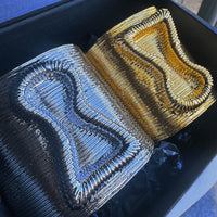 Two embroidered fabric samples, one blue and one gold, on a black background.