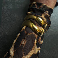 Gold bracelet on a wrist with a leopard print sleeve against a dark background